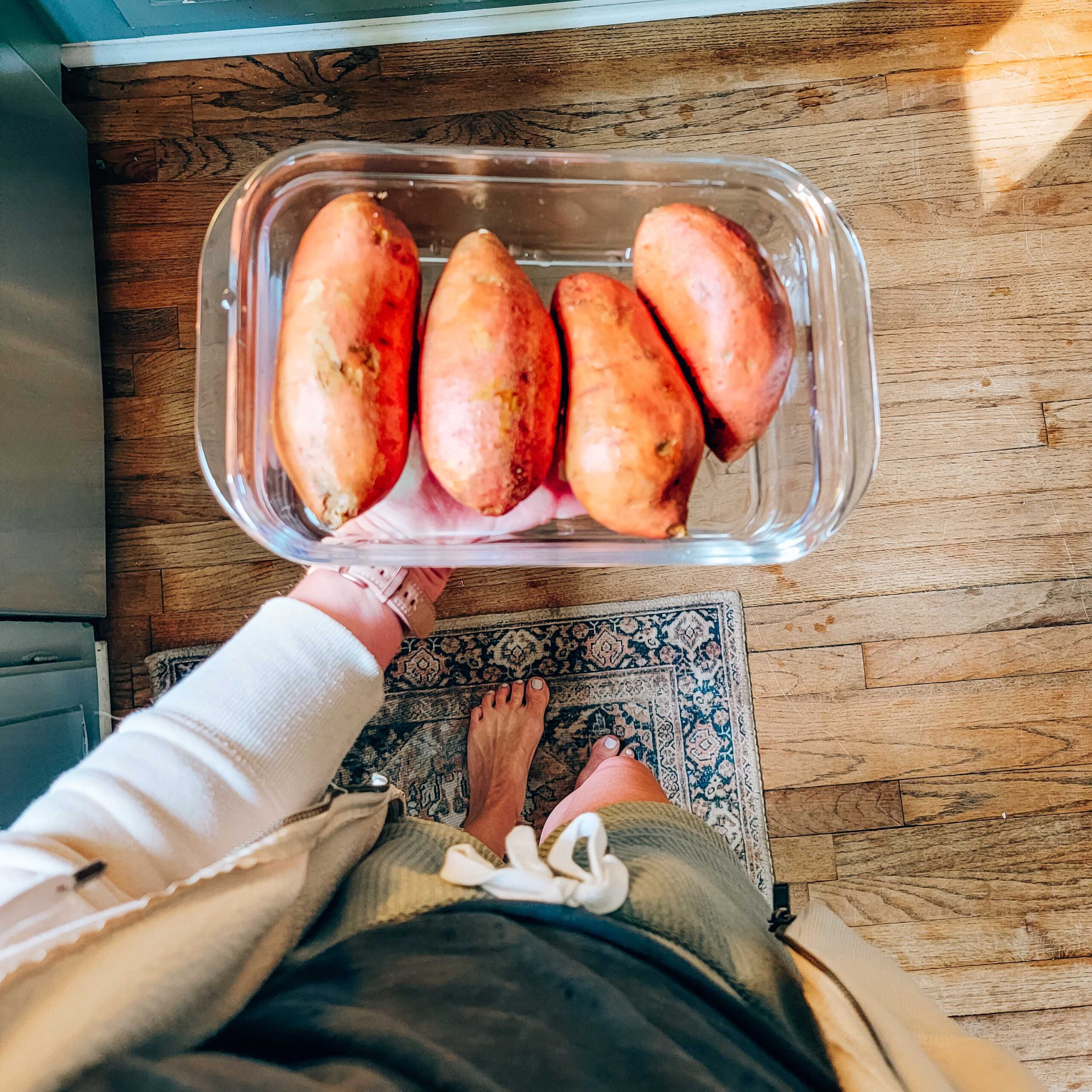 Woman holds sweet potatoes in glass tupperware. 