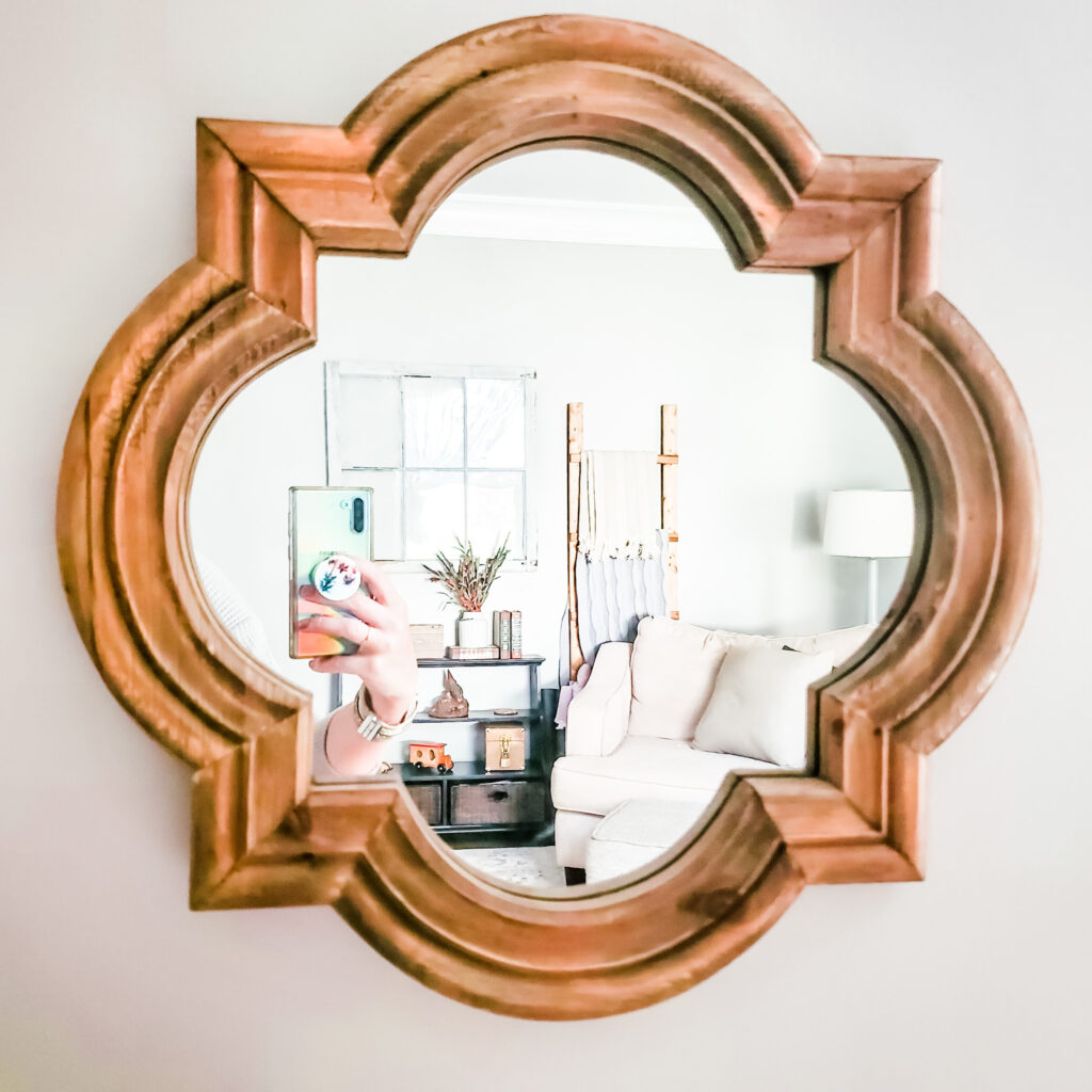 Picture of mirror reflects cozy living room with armchair and blanket ladder. 