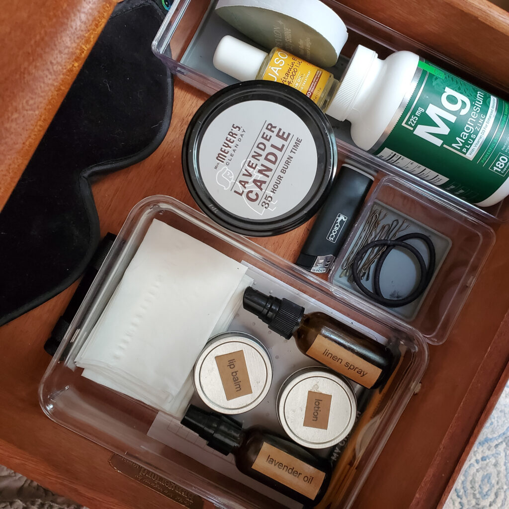 Organized nightstand drawer with hair supplies, candle, lip balm, scented spray, tissues, and eye masks. 